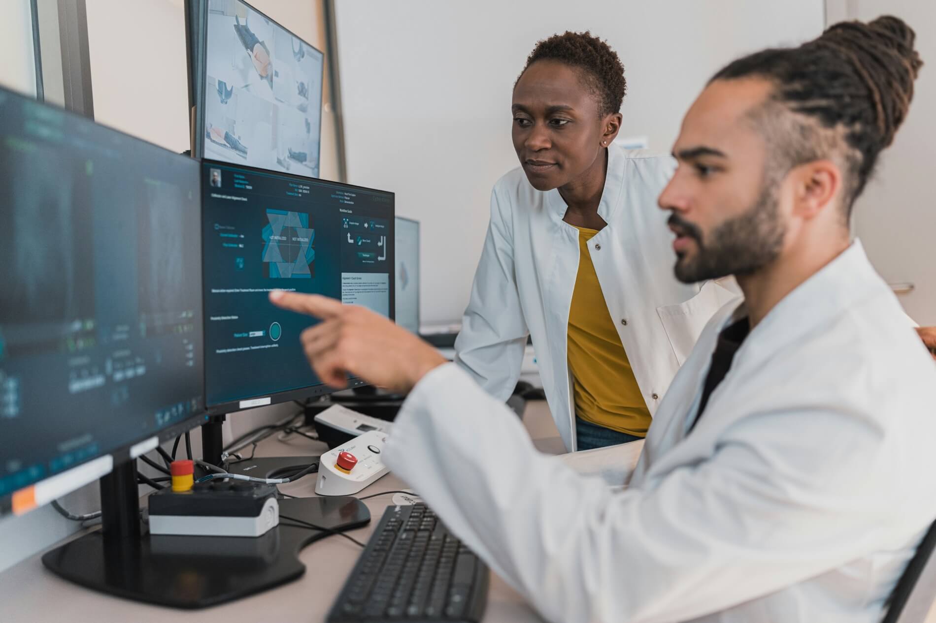 Two professionals discussing data on multiple computer monitors in an office.