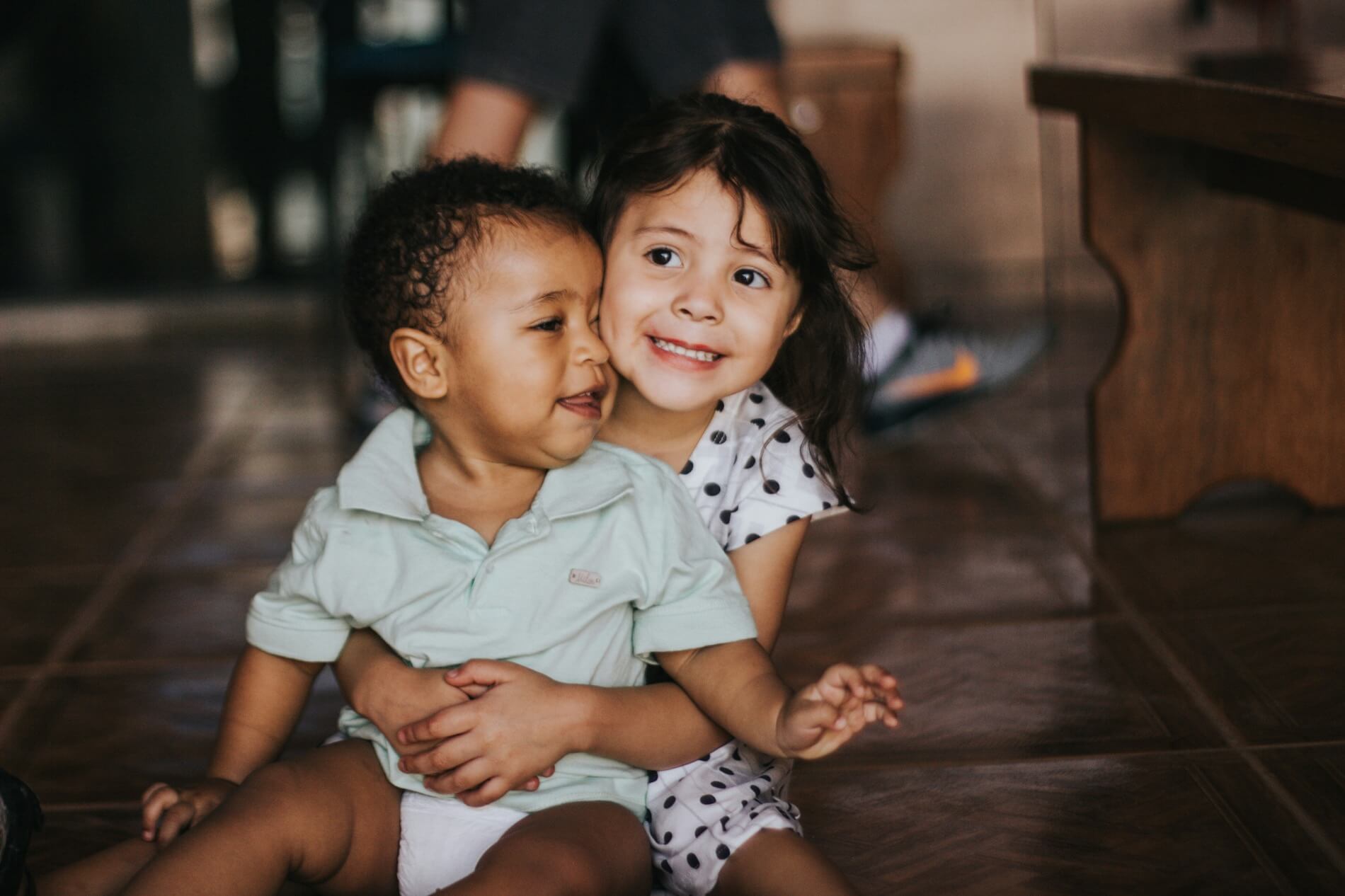 Young girl embracing a baby sitting on the floor indoors