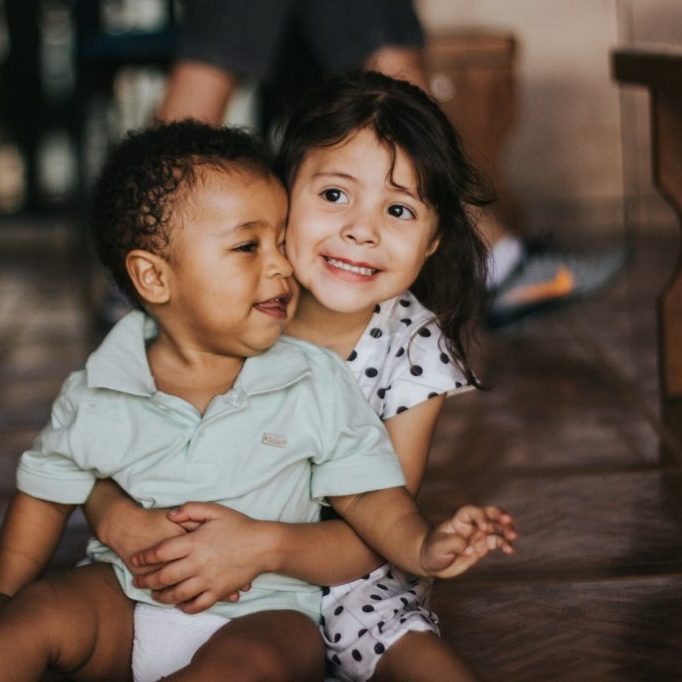 Young girl embracing a baby sitting on the floor indoors