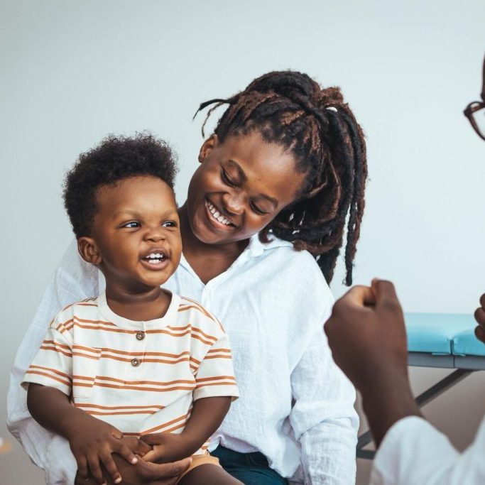 A doctor conversing with a mother and her young child in a clinic.